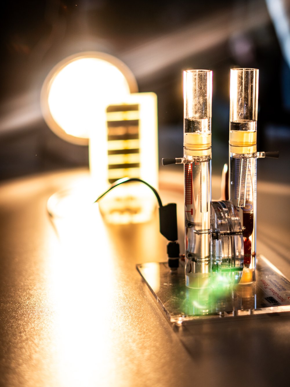 Nahaufnahme eines Wasserstoff-Versuchsaufbaus mit einer hellen Lampe und zwei Röhren mit Flüssigkeit.