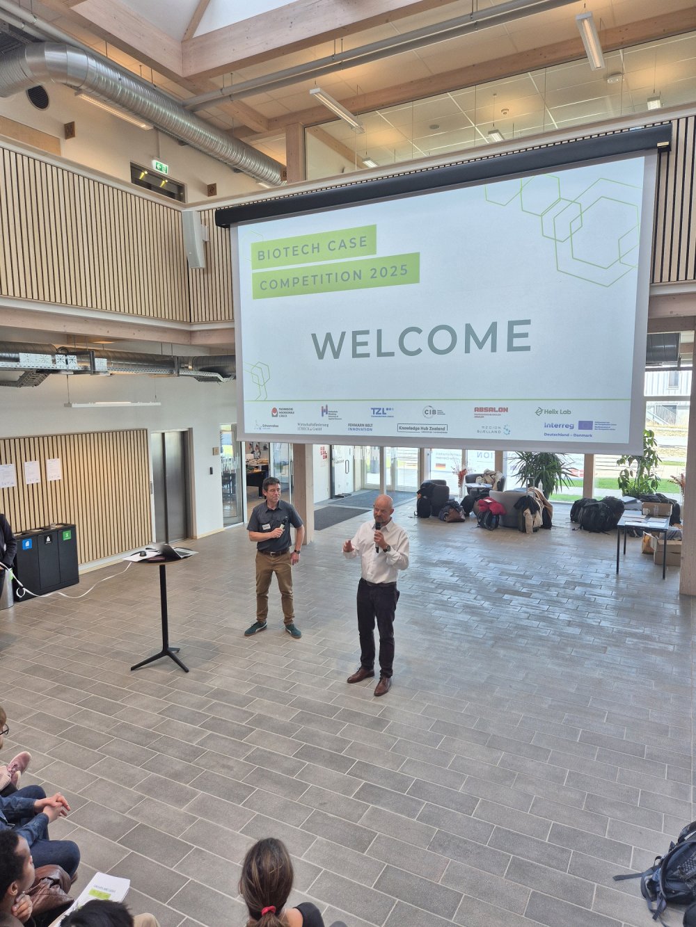Auf einer Bühne stehen zwei Männer vor einer Leinwand mit großer Aufschrift &quot;Welcome&quot;