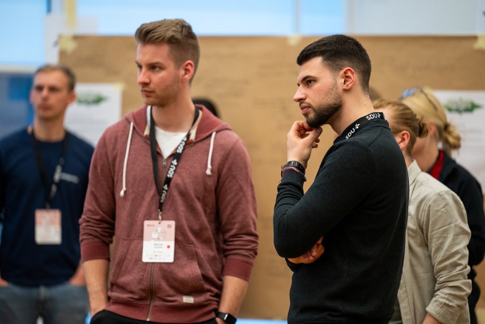 Zwei junge Männer stehen zusammen und blicken konzentriert auf etwas außerhalb des Bildrandes.