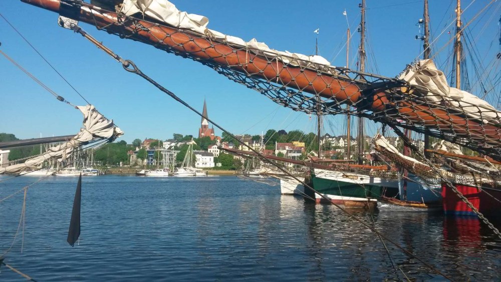 Bild vom Flensburger Hafen im Sonnenschein, mit der Takelage eines alten Segelschiffes im Vordergrund.