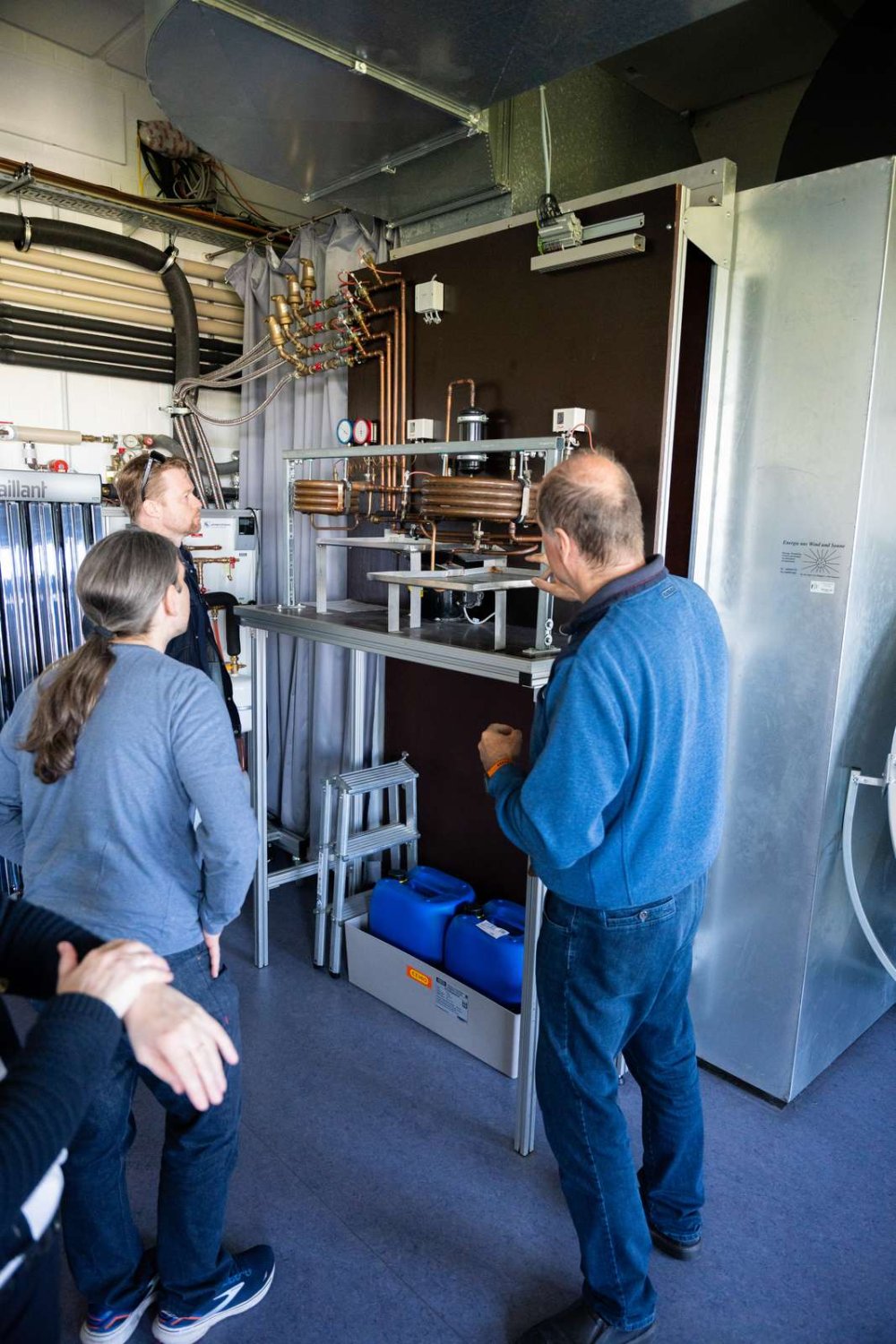 Ein Mann erklärt einem anderen Mann und einer Frau eine Brennstoffzellen-Anlage.