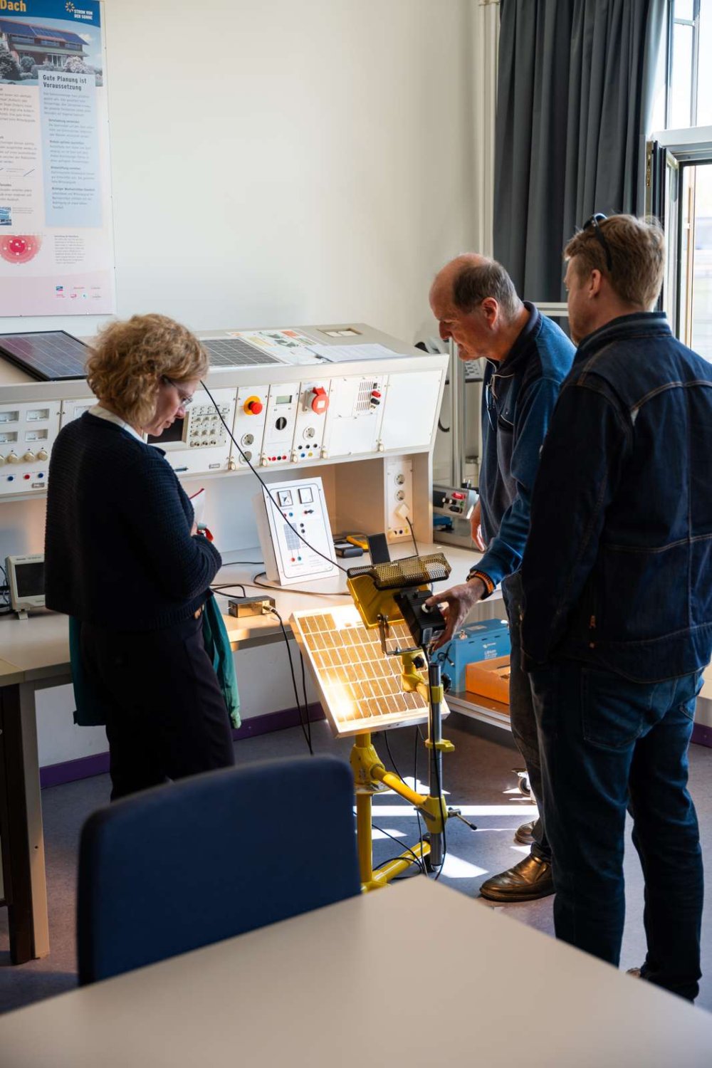 Zwei Männer und eine Frau betrachten einen Versuchsaufbau mit einer Brennstoffzelle.