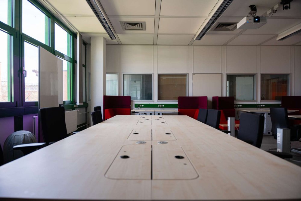 PC-Laborraum mit einem großen Tisch, bunten Sitzecken und Bürostühlen.