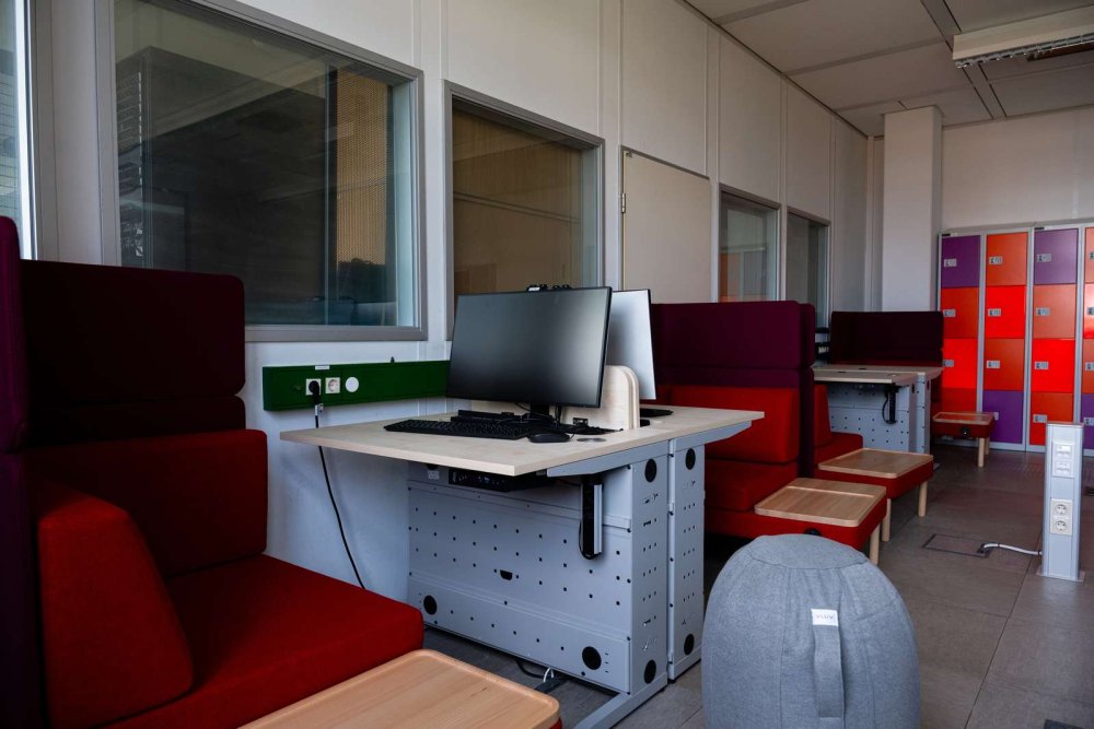 PC-Arbeitsplätze mit roten Sitzecken und buten Schließfächern im Hintergrund.