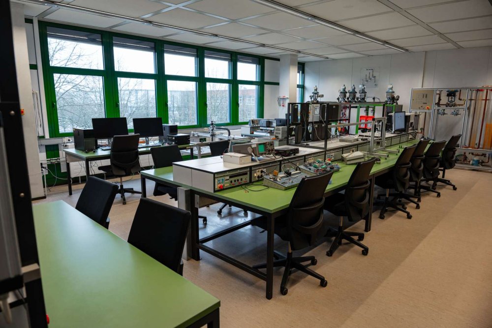 Das Bild zeigt die Ausstattung eines regelungstechnischen Labors mit mehreren Arbeitsplätzen. Auf den Arbeitstischen stehen Oszilloskope, Monitore, Netzgeräte und weitere elektronische Geräte. Die Geräte werden für praktische Experimente zur Regelung von technischen Systemen genutzt.