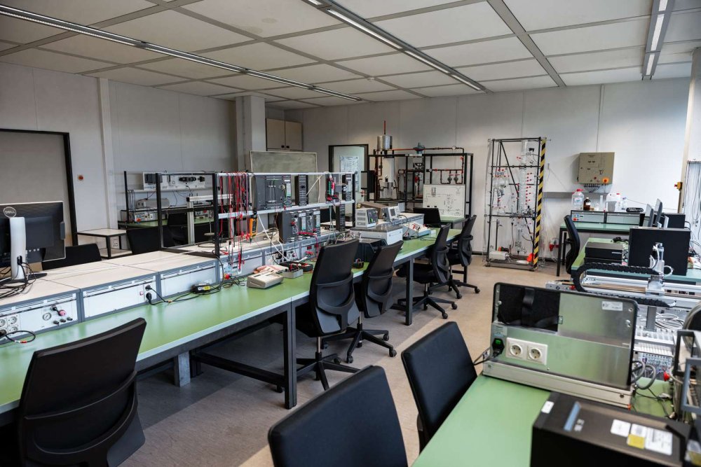 Das Bild zeigt die Ausstattung eines regelungstechnischen Labors. Auf den Arbeitstischen stehen Oszilloskope, Monitore, Netzgeräte und weitere elektronische Geräte. Die Geräte werden für praktische Experimente zur Regelung von technischen Systemen genutzt.