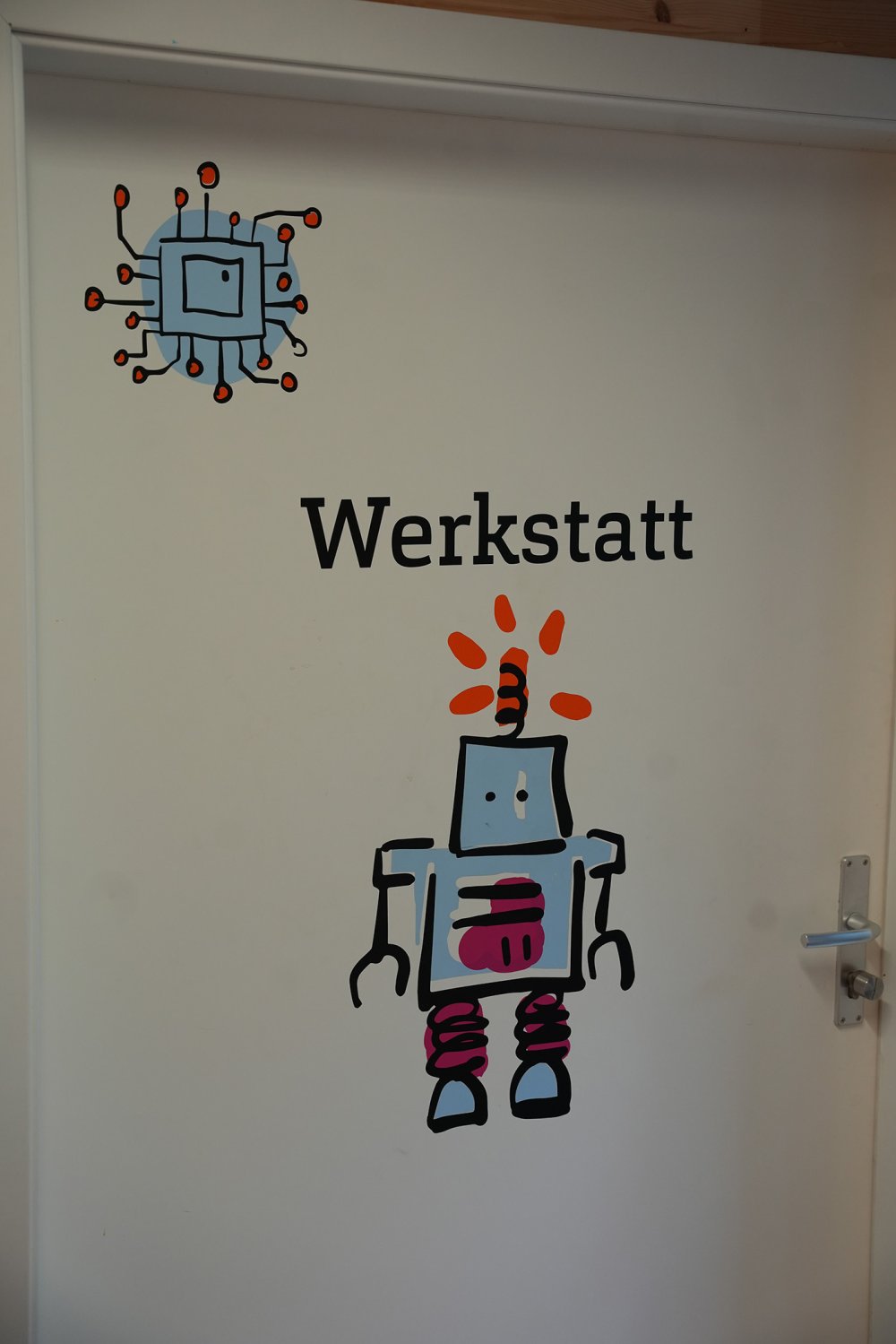 Weiße Tür mit Aufdruck: Werkstatt und Zeichnung eines Roboters.