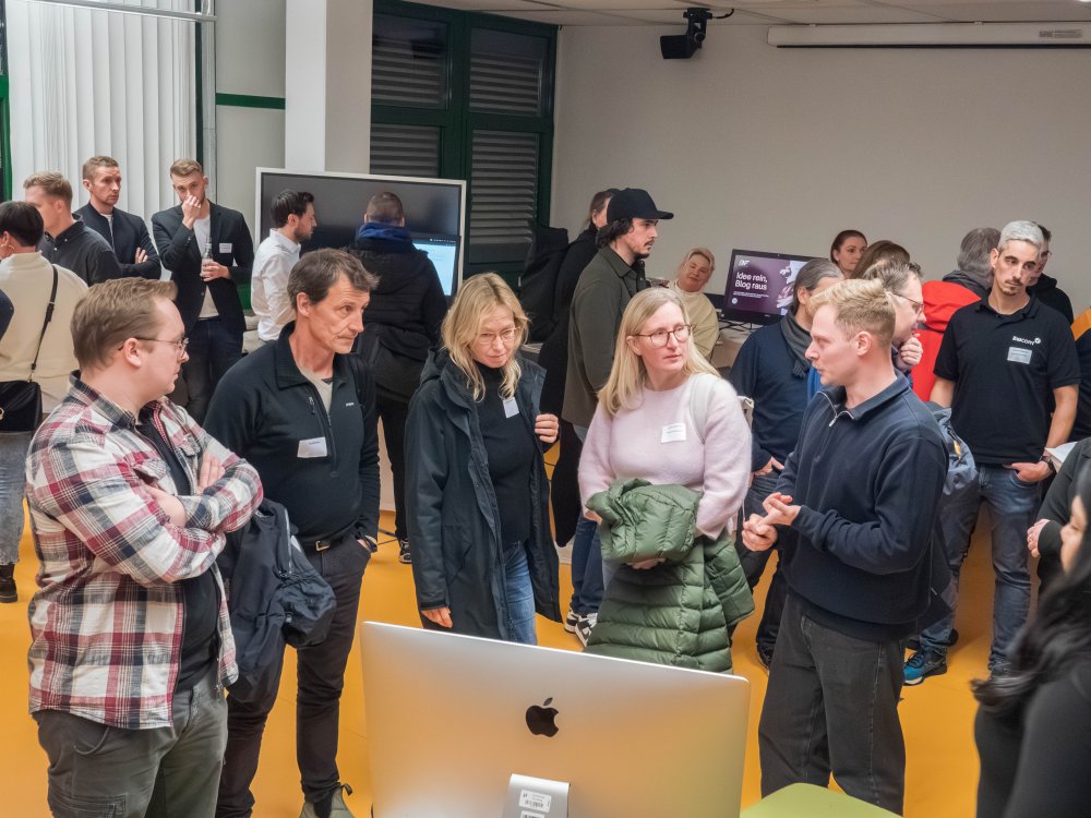 Viele Mensxchen stehen in einem Raum mit Computern und unterhalten sich. 