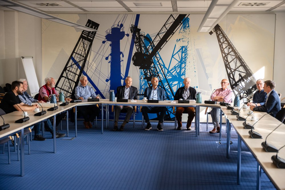 Viele Männer sitzen an einem u-förmigen Tisch