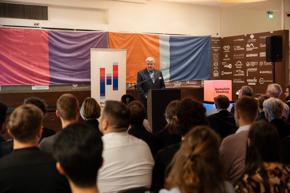 Ein Redner am Pult im Vordergrund verschwommen erscheinende MEnschen