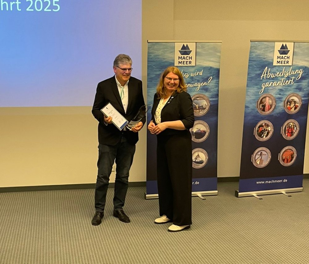 Ein Mann und eine Frau stehen auf einer Bühne. Sie übergibt ihm eine Urkunde