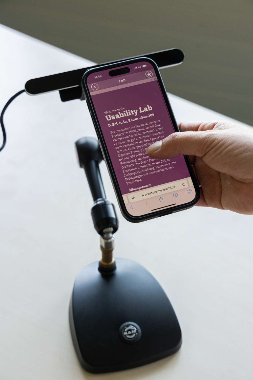 Nahaufnahme eines Handys auf einem Handy-Standhalter, darauf Überschrift &quot;Usability Lab&quot; und weiterer Text, eine Hand swipt nach oben.