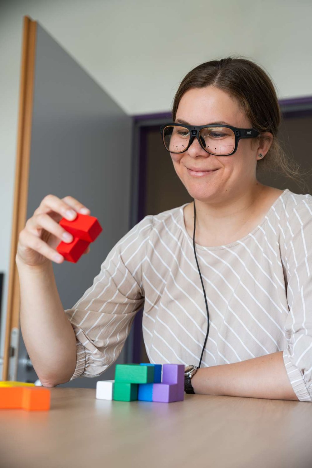 Eine Frau trägt eine Eye-Tracking-Brille und betrachtet damit bunte Klötze, die vor ihr liegen.