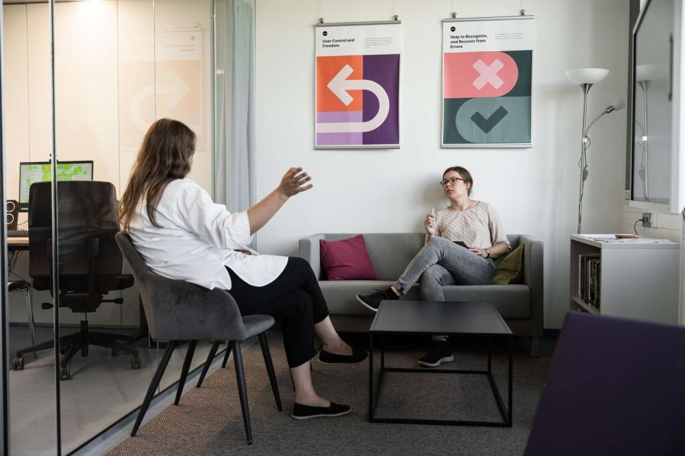 In einem Laborraum sitzen zwei Frauen in einer Sitzecke mit Sofa und unterhalten sich.