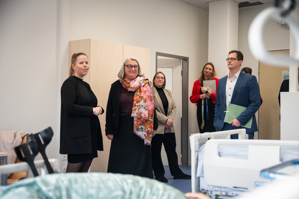 Zwei Frauen im Vordergud, mehre Menschen im Hintergrund, die in einem Raum stehen