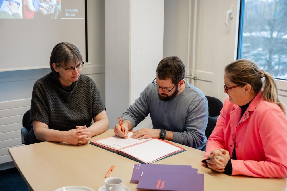 Ein mann ziwschen zwei Frauen die am Tisch sitzend Urkunden unterschreiben