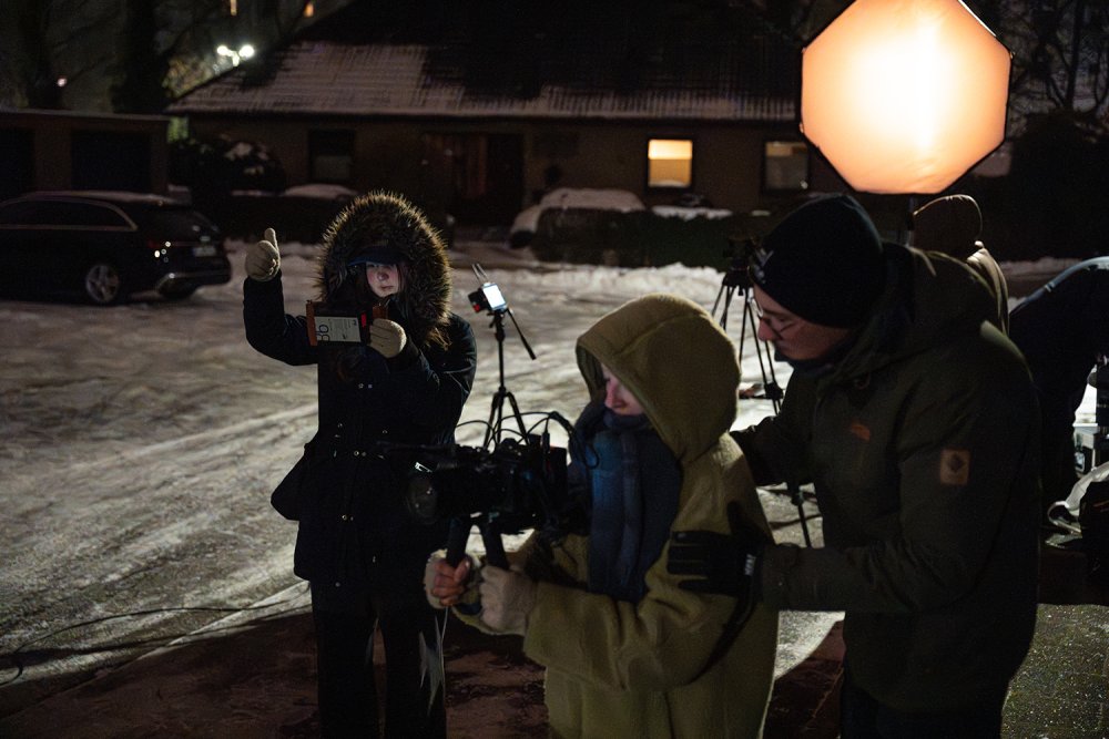 Eine Gruppe von Studierenden bei einem Filmdreh auf einer winterlichen Straße, eine zeigt mit Blick auf die Kamera den Daumen hoch.