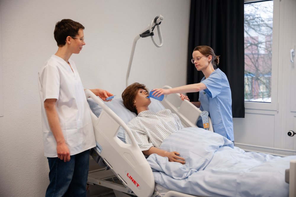 Eine Frau gibt einer Puppe, die aussieht wie ein echter Mensch, was zu trinken. eine andere frau schaut zu. 