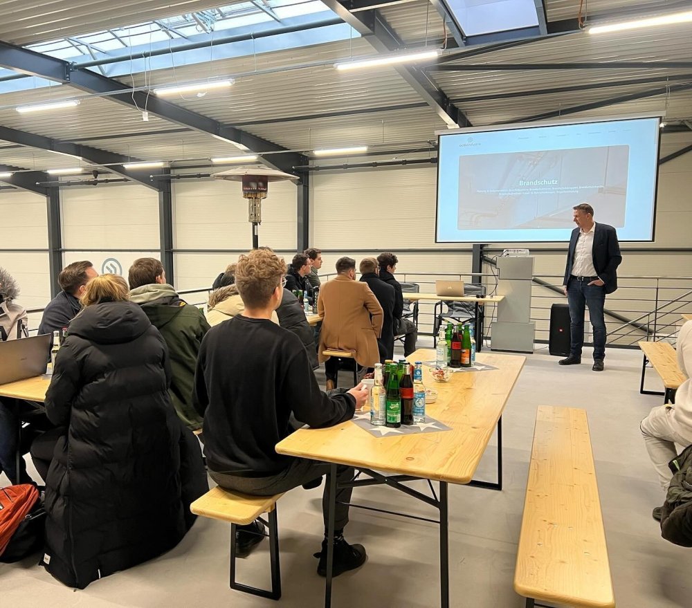 Menschen sitzen an Tischen und schauen auf eine Leinwand