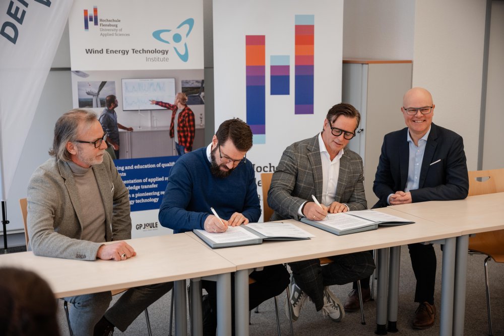 Vier Männer sitzen am Tisch und unterschreiben einen Vetrag.