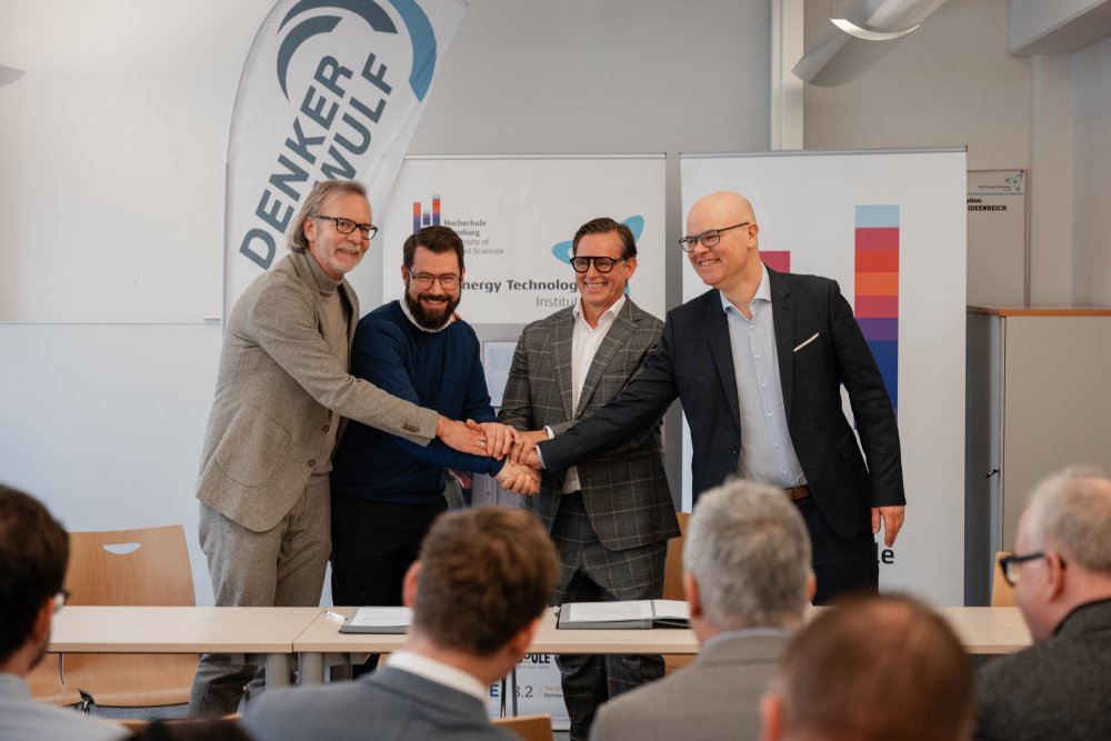 Vier Männer sitzen am Tisch und unterschreiben einen Vetrag.