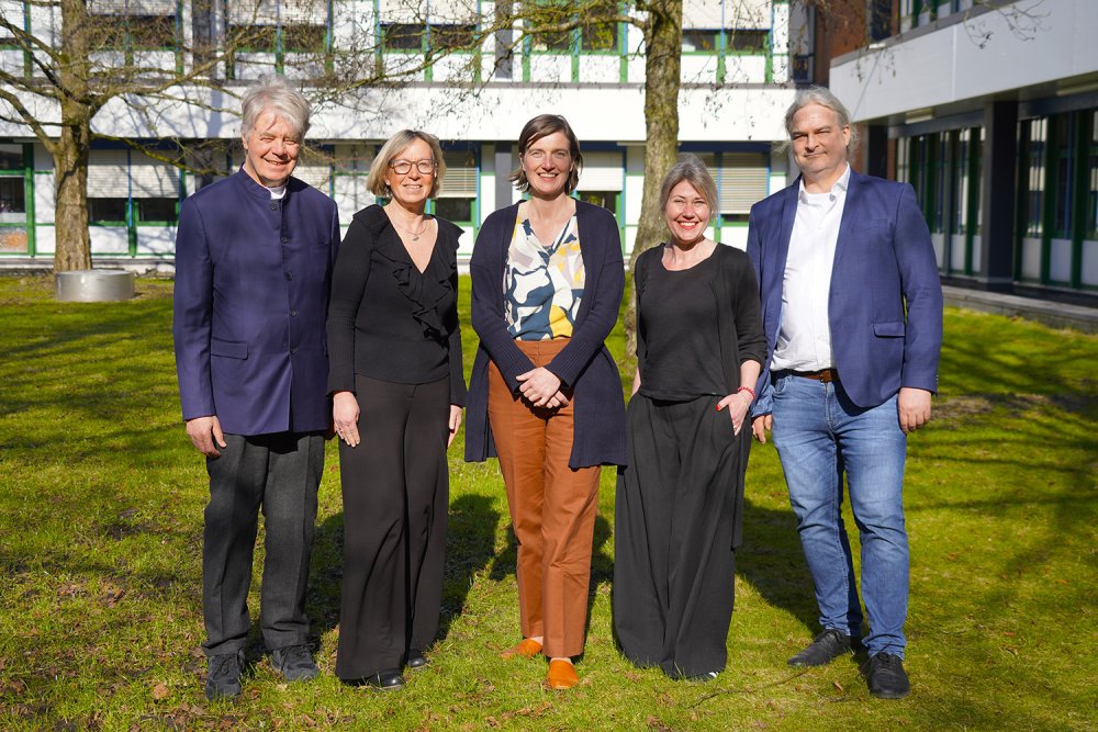 Der Hochschulrat der Hochschule Flensburg (v.l.: Klaus Joachim Scheunert, Petra Nicolaisen, Dr. Conny Clausen, Maike Rotermund und Achim Englert) stehen im Sonnenschein auf einer grünen Wiese vor einem Hochschulgebäude und lächeln in die Kamera.