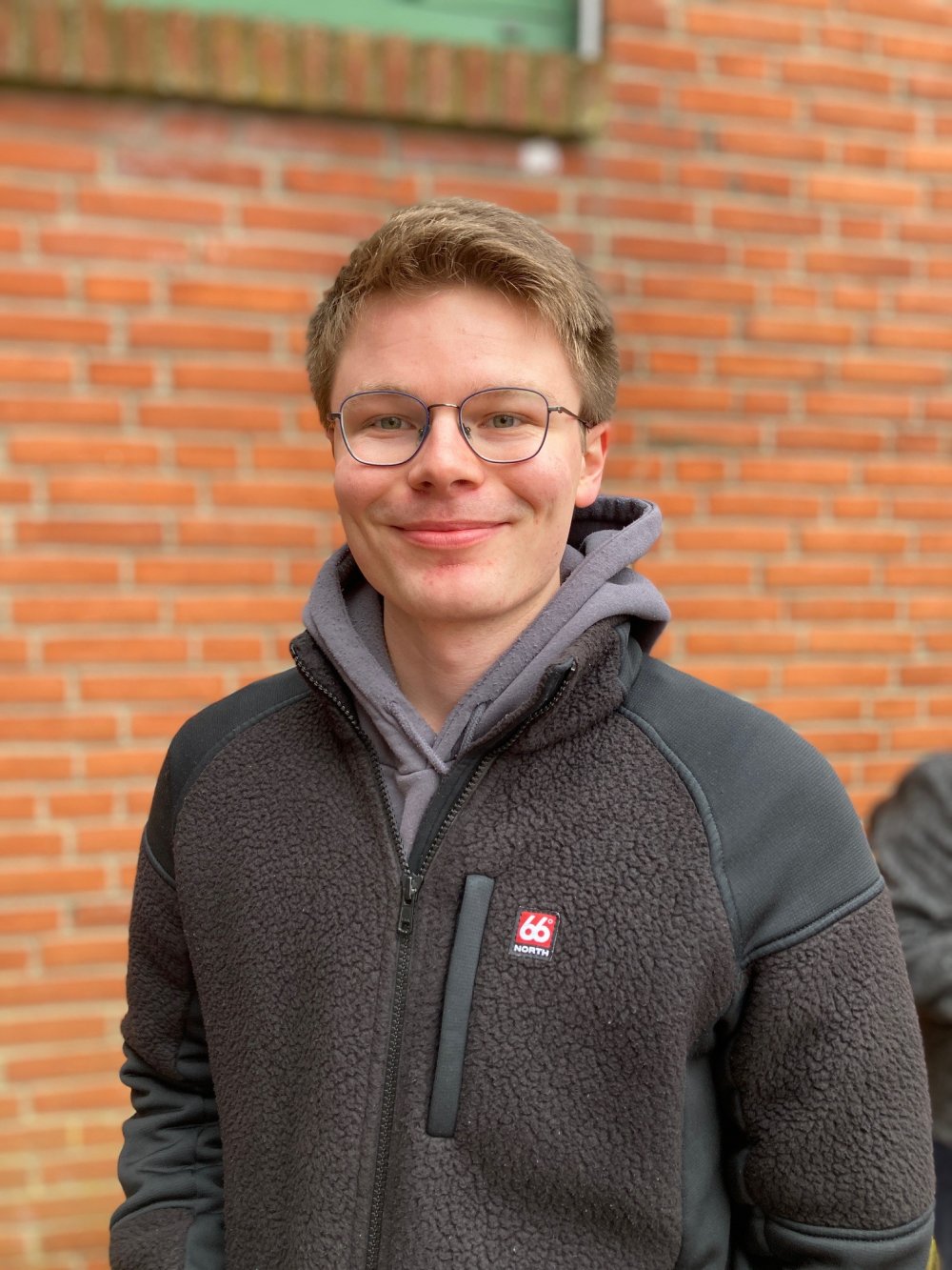 Ein junger Mann mit Brille vor roter Ziegelwand