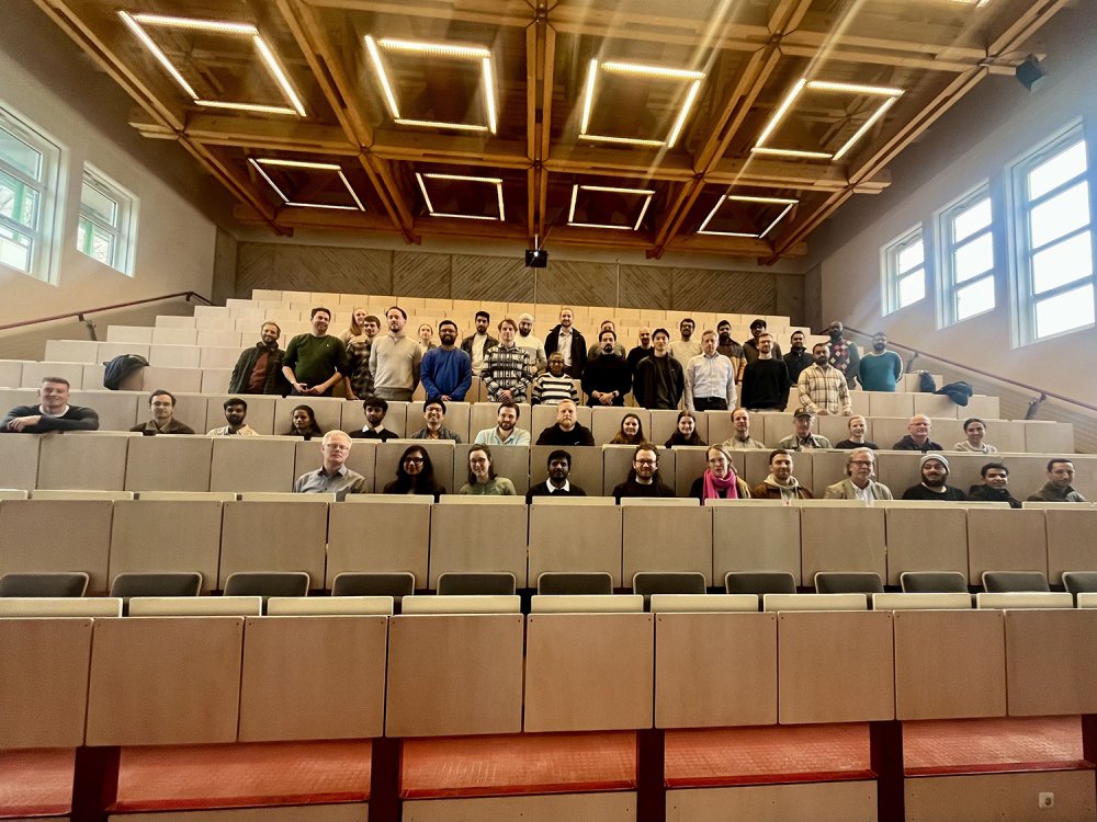 Sitzreihen in einem Vorlesungssaal, eine Gruppe von ca. 30 Menschen lächelt in die Kamera.