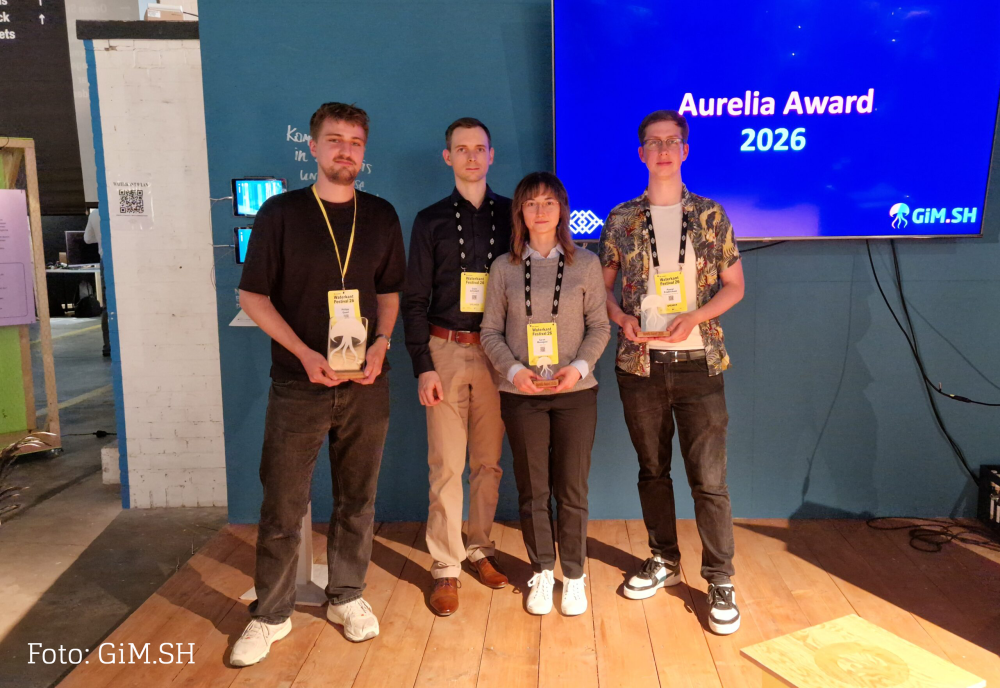 Vier junge Menschen halten Pokale in der Hand, hinter Ihnen ein Monitor mit Text: Aurelia Award 2026, GiM.SH