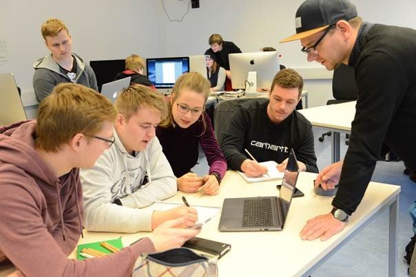 Eine Gruppe Studierender arbeitet an einem Tisch sitzend. Vor ihnen liegt ein Tablet im Hintergrund sind Computer zu erkennen.
