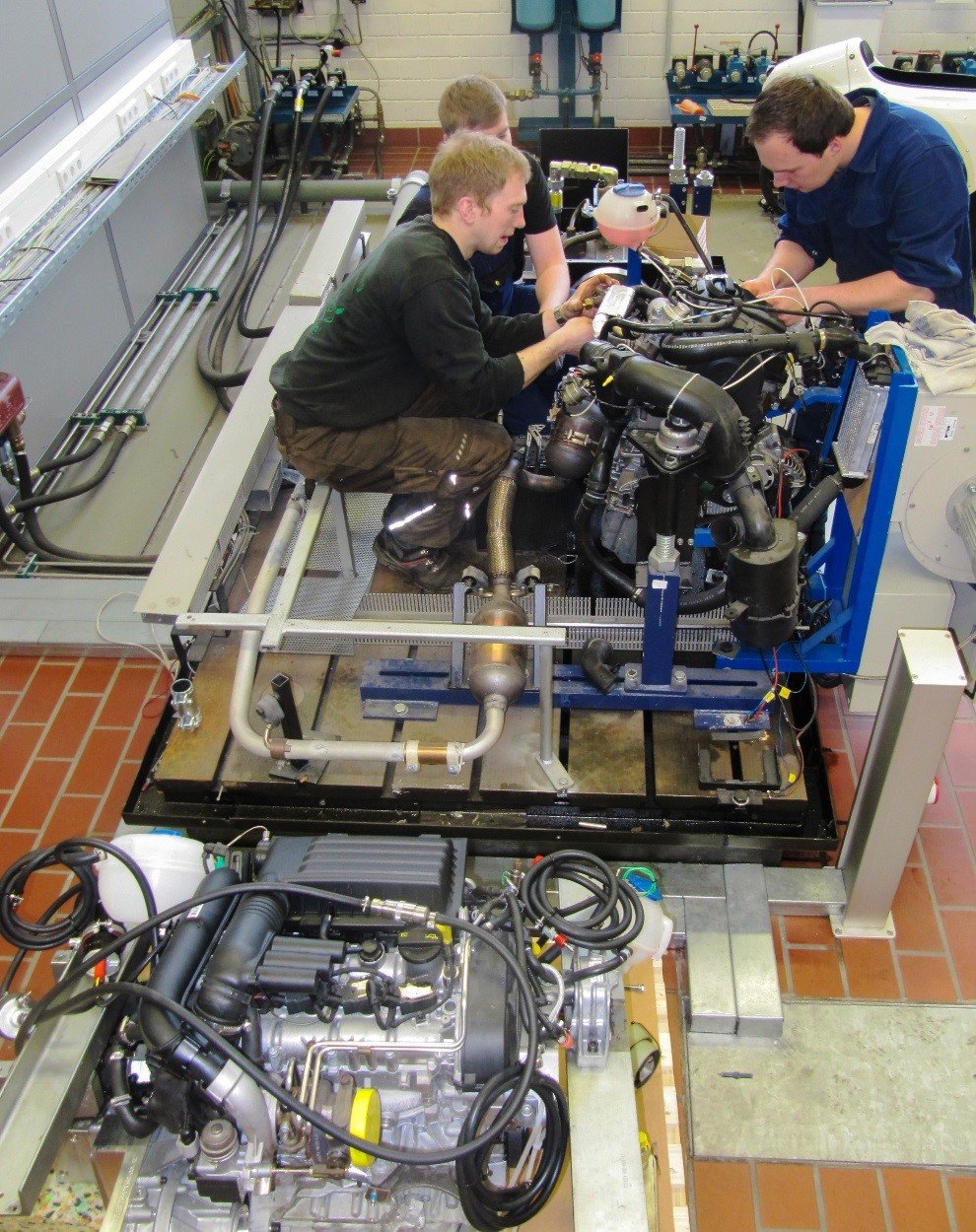 Die Maschinenbaustudenten Nicolay Tank, Lukas Klink und Christoph Jensen beim Abbau des in die Jahre gekommenen Prüfstandsmotors. Im Vordergund der neue 1,4 TSI Turbomotor. 