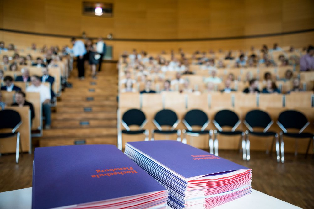 Blick in die Zuschauerreihen, vorn im Bild zwei Stapel Mappenin Hochschulfarben.