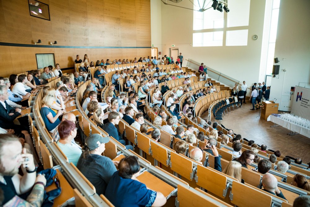 Blick ins Publikum von schräg hinten, einige suchen noch nach Plätzen.