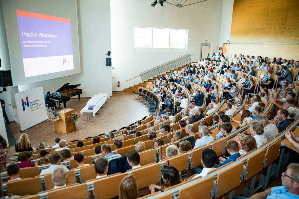 Das Publikum von hinten, unten spielt ein Mann Klavier.
