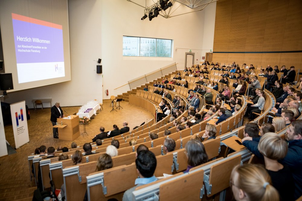 Blick von hinten: Erst Publikum, dann Präsident am Rednerpult und Hochschulaufsteller und Präsentation.