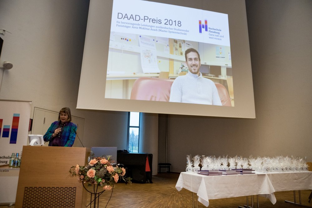 Mitarbeiterin des International Office am Rednerinnenpult, hinter ihr an die Wand projiziert: Bild eines Studenten und Überschrift "DAAD Preis 2018".