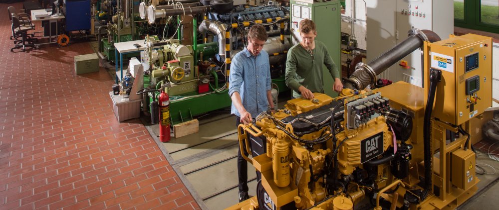 Zwei Studenten in der Maschinenhalle arbeiten an einer Baumaschine.