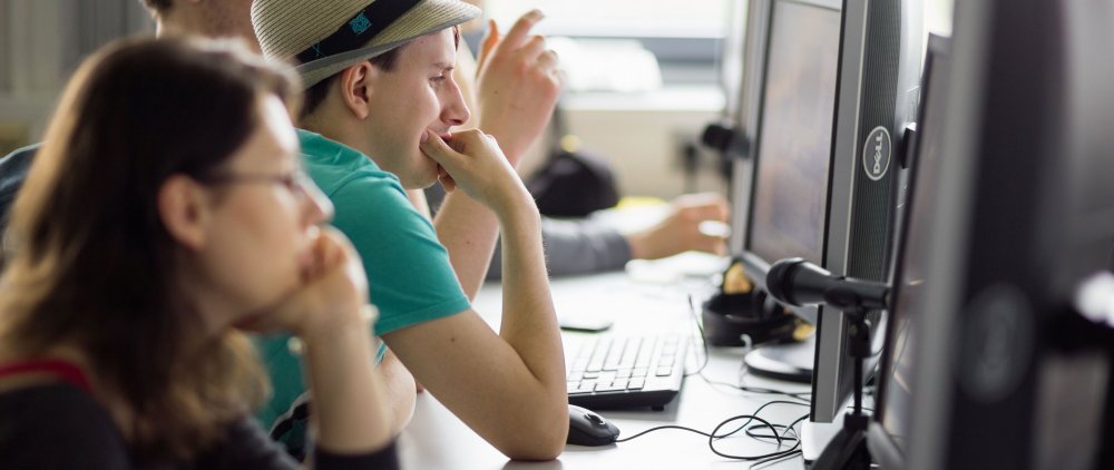 Studierende sitzen nebeneinander in einer Reihe im PC-Labor und arbeiten je an einem Rechner.