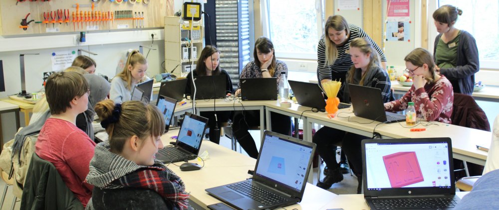 Mädchen sitzen um einen Tisch und arbeiten an Computern.