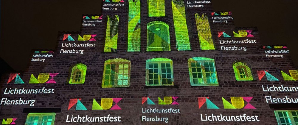 Lichtprojektion auf eine Backsteinfassade: Logo und Name des Lichtkunstfest Flensburg.