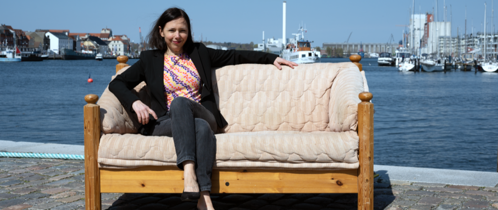 Angela Clemens sitzt auf einem Sofa, das am Flensburger Hafen steht.