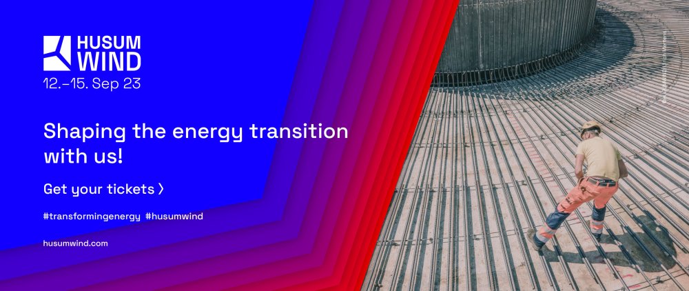 A man in workwear stands on a concrete surface covered with metal braces which are ararnged in a radial manner. On the left you can read the following: "Husum Wind - 12.-15. Sep 23 - Shaping the energy transition with us! - Get your tickets - #transformingenergy #husumwind - husumwind.com"