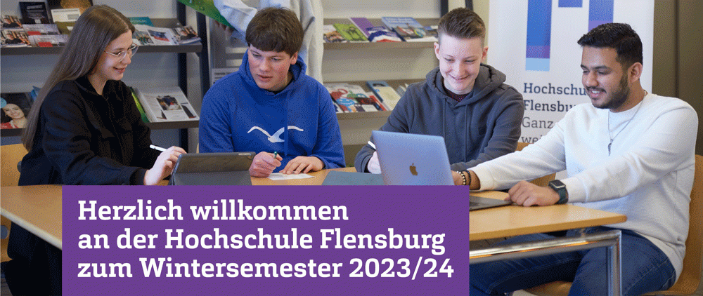 Drei Studenten und eine Studentin sitzen um einen Tisch im Foyer der Hochschule. Ein violetter Balken trägt die Aufschrift "Herzlich willkommen an der Hochschule Flensburg zum Wintersemester 2023/24"