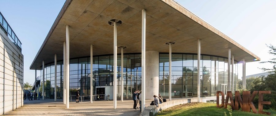 Das audimax-Gebäude auf dem Flensburger Campus, seitlich steht das Wort "Danke" in Großbuchstaben aus Metall auf einer Wiese.