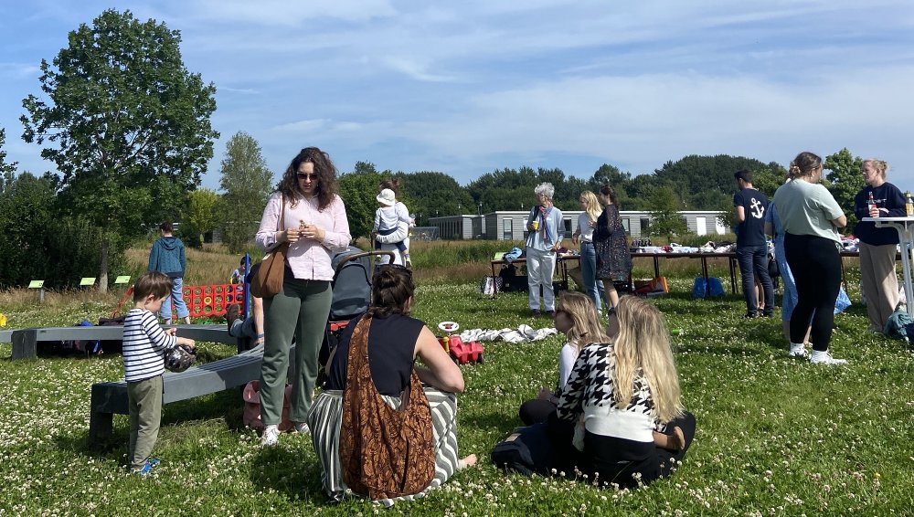 Eine Gruppe von jungen Erwachsenen und kleinen Kindern auf einer grünen Wiese mit blauem Himmel darüber.