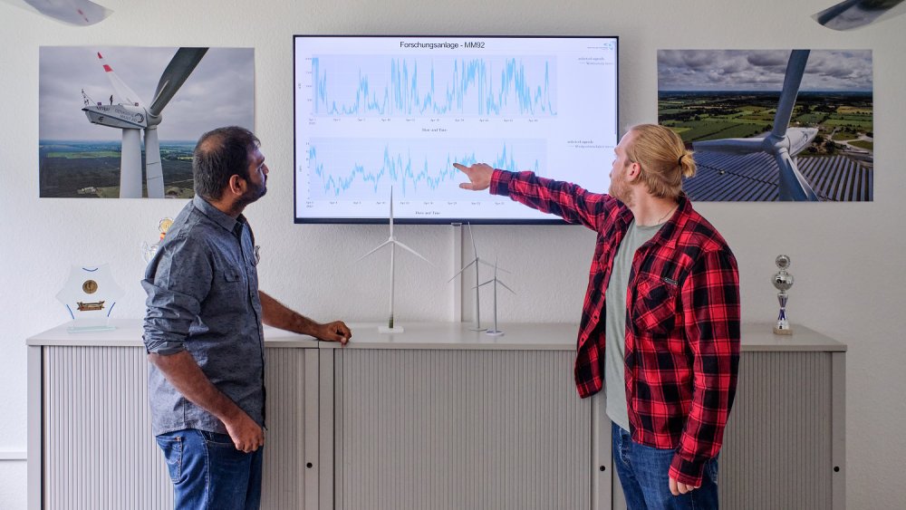 Zwei Studenten stehen vor einem Monitor, auf den einer von ihnen zeigt.