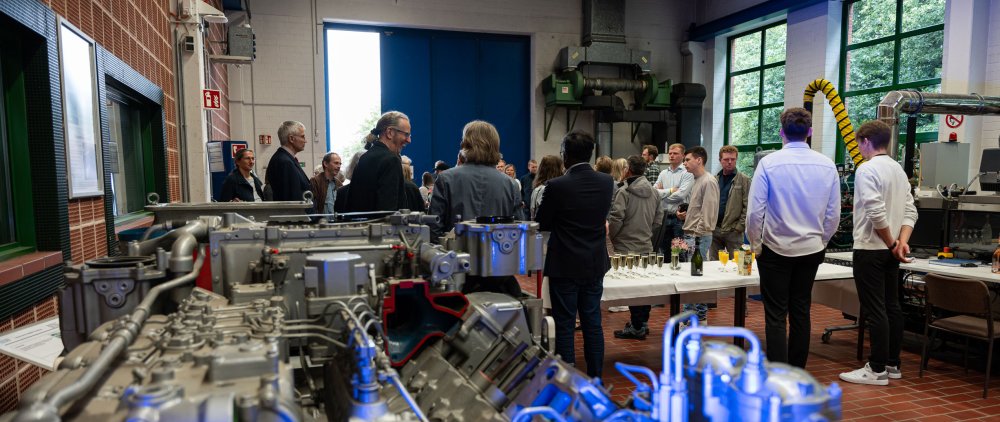 Event in an engine and machine hall: There is a big piece of equipment. In the background you can see people talking.
