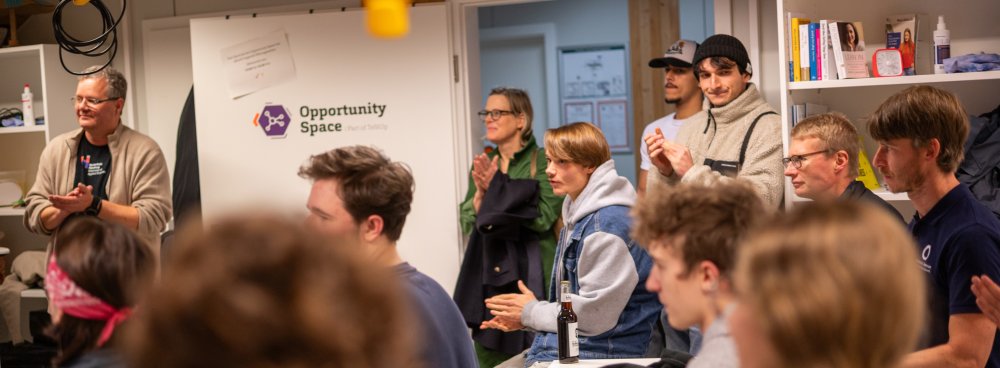 In einem Seminarraum sitzen und stehen Studierende und applaudieren.