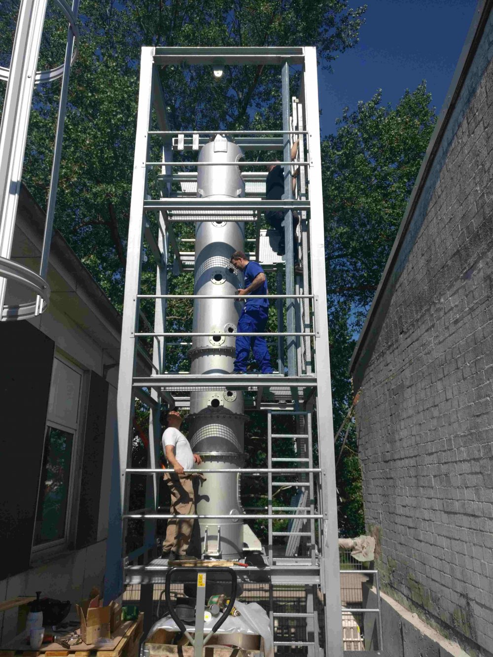 Ein Metallgerüst, links und rechts davon Mauern. Im Gerüst steht der zylinderförmige Turm aus dem vorherigen Bild.