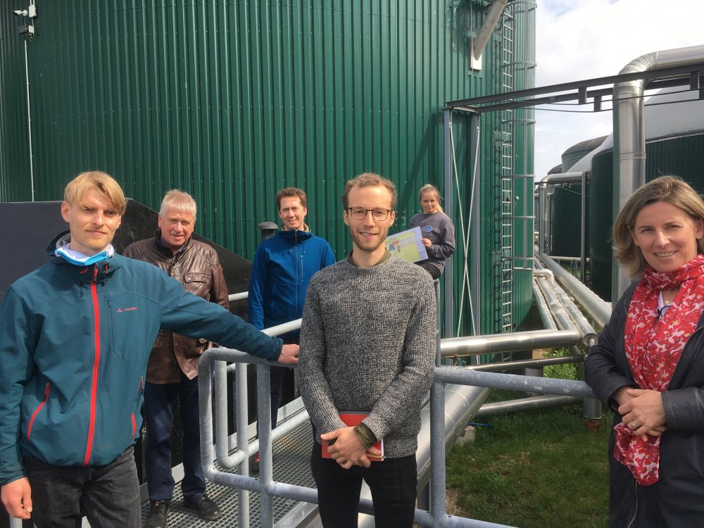 Eine Gruppe Menschen steht vor einer grünen Wand aus Metall und einer gerüstähnlichen Struktur.